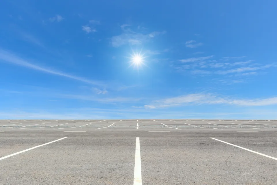 Vast, empty parking lot with blue sky and bright sun in background